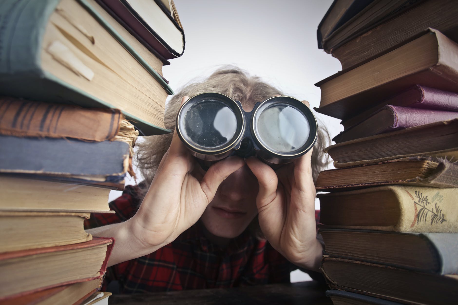 person with binoculars behind books